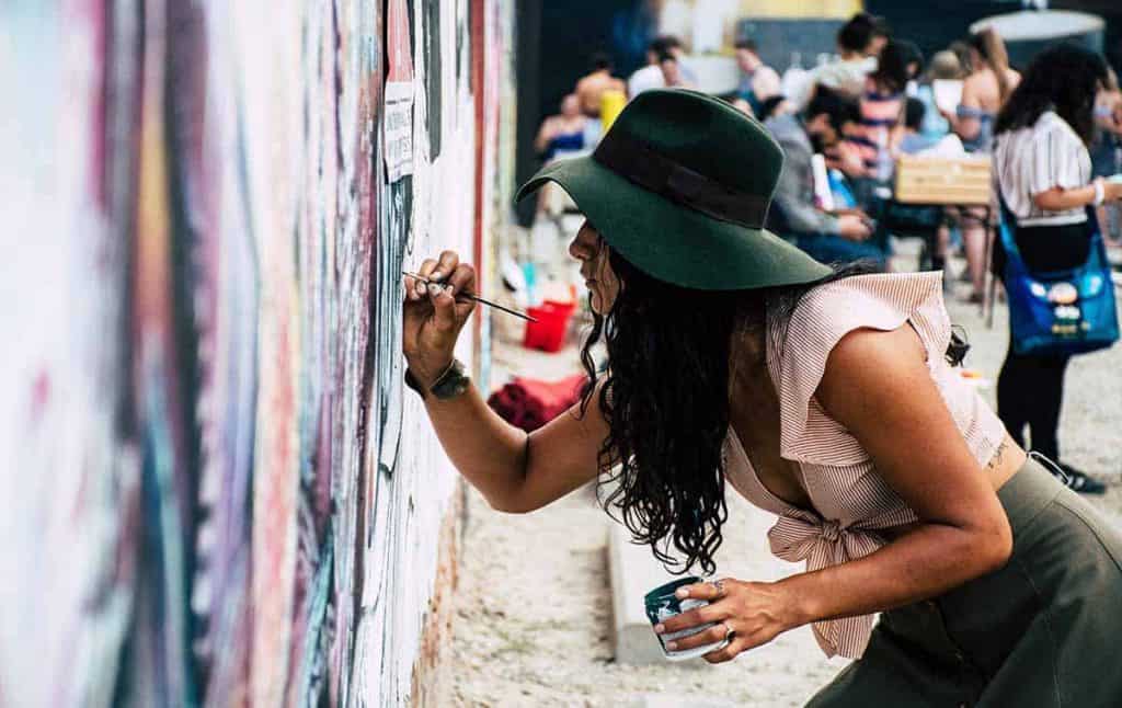 Une femme porte un chapeau et peint une murale à l'aide d'un pinceau