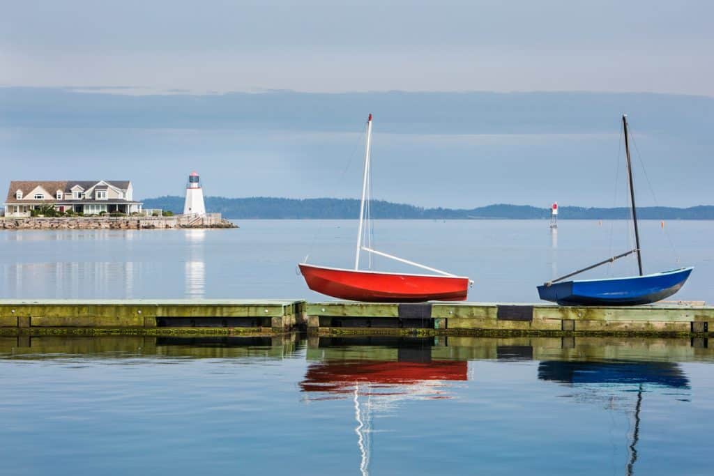 Un quai et deux petites embarcations de pêche. Au loin un phare blanc.