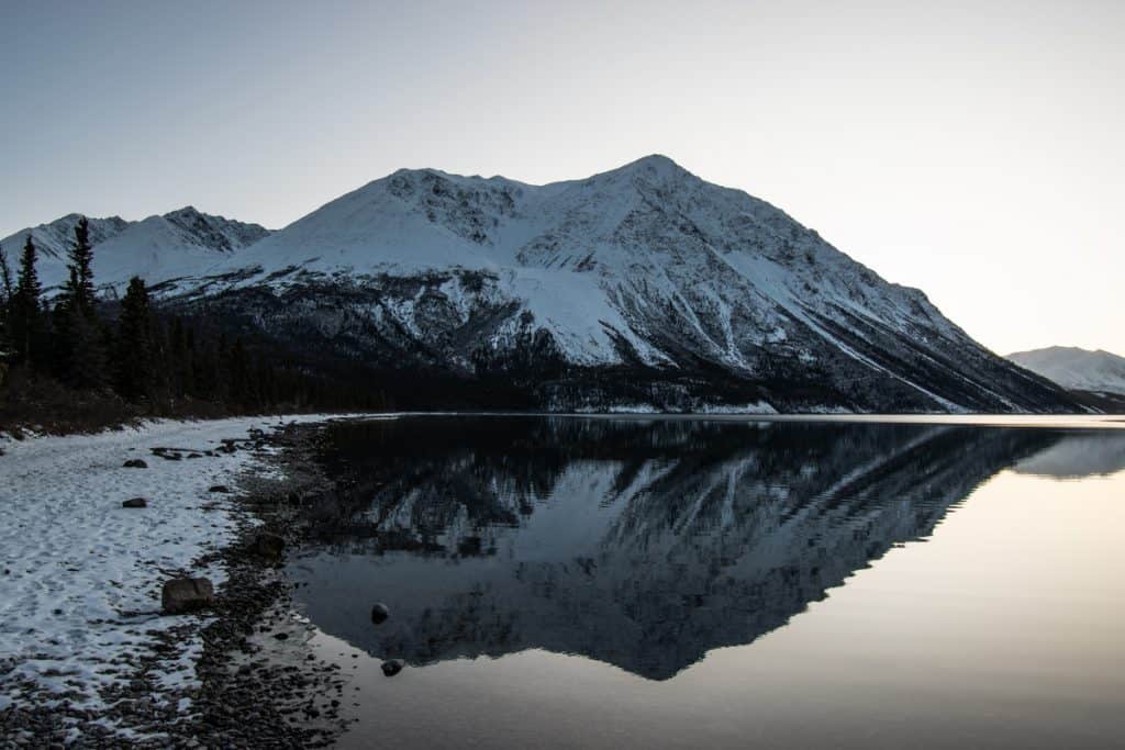 Paysage nordique. Une grande montagne enneigée et des sapins à côté d'un lac.