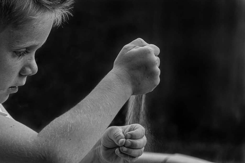 Un garçon verse du sable sur sa main gauche à l'aide de sa main droite.